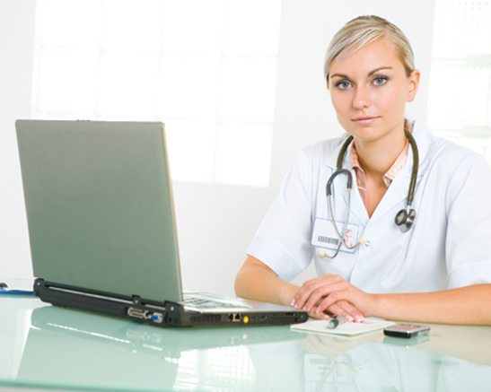 Woman in medical clothing sitting at a laptop