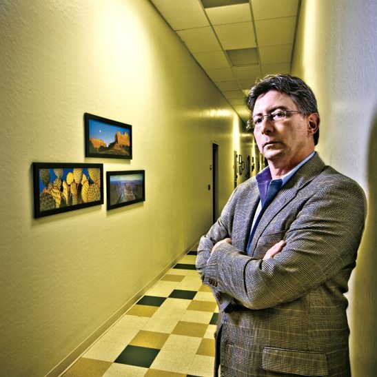 Man standing in foreground of yellow hallway with photographs on opposite wall