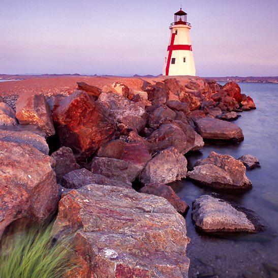 Looking over rocks towards a replica lighthouse at sunrise