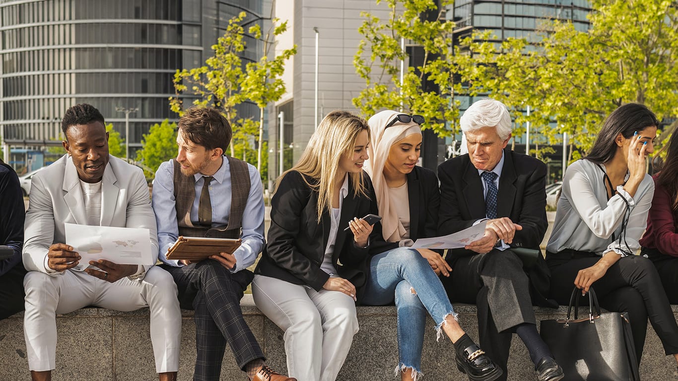 Diverse businessmen and businesswomen, sitting outside an office building taking a break together, people of different ages and different countries, multiracial, co-workers.