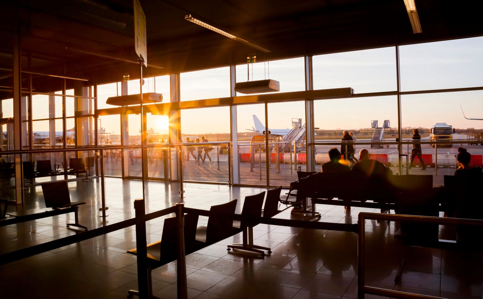 Silhouette of airline passengers in a regional airport lounge by sunset.