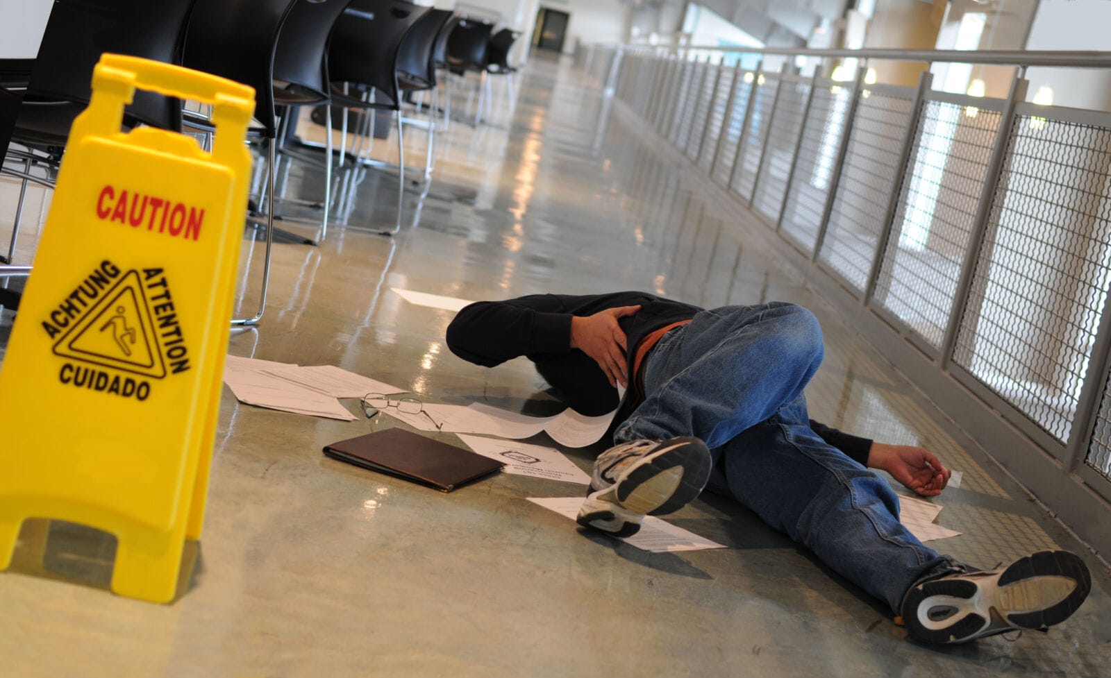 A man who slipped on a wet floor beside a bright yellow caution sign holds his back in pain.