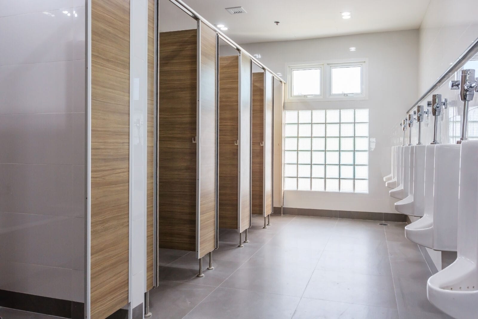 White urinals in clean men public toilet room empty with big window and light from outside, interior.