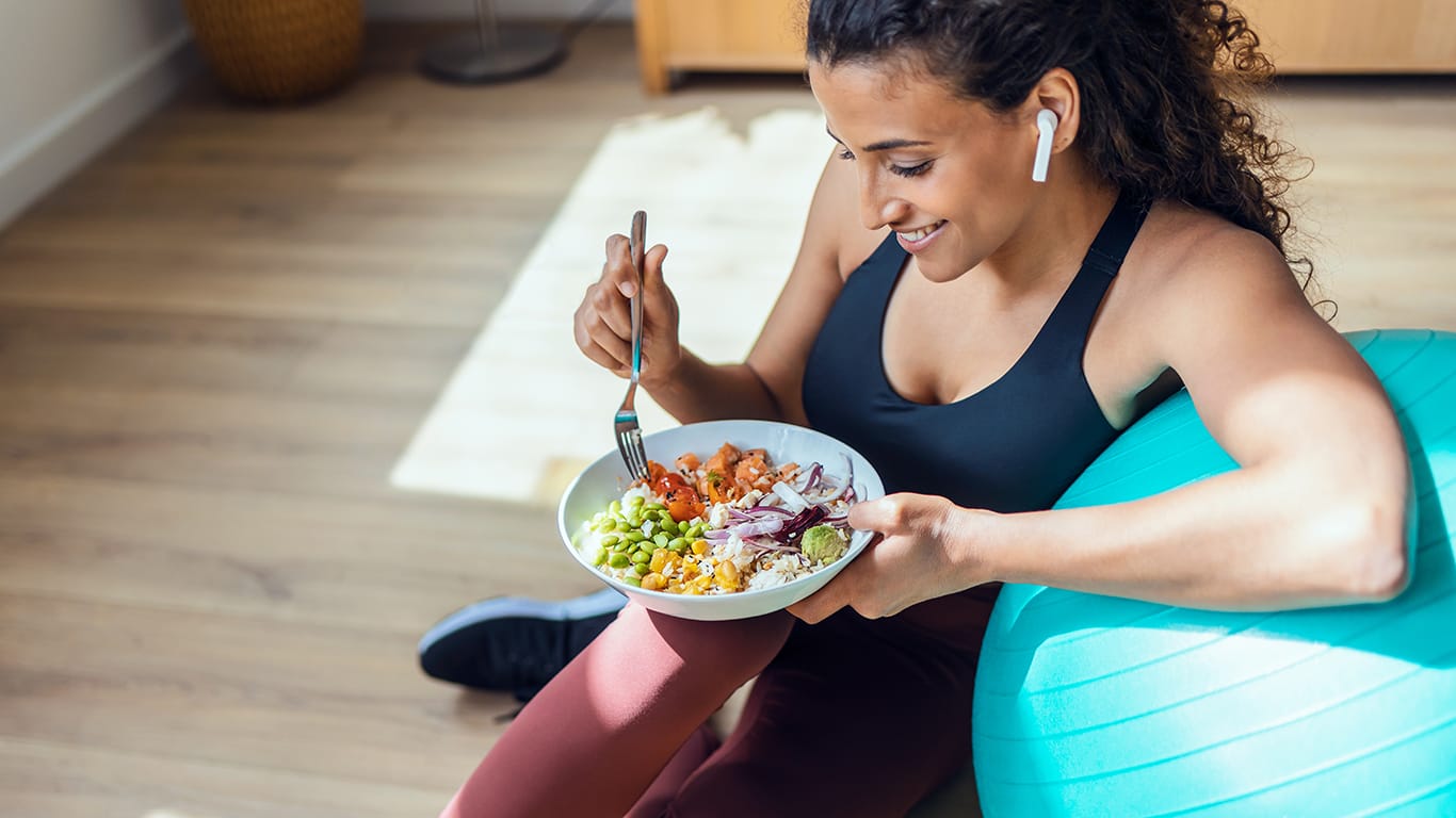 Shot of sporty young woman eating healthy while listening to music sitting on the floor at home.