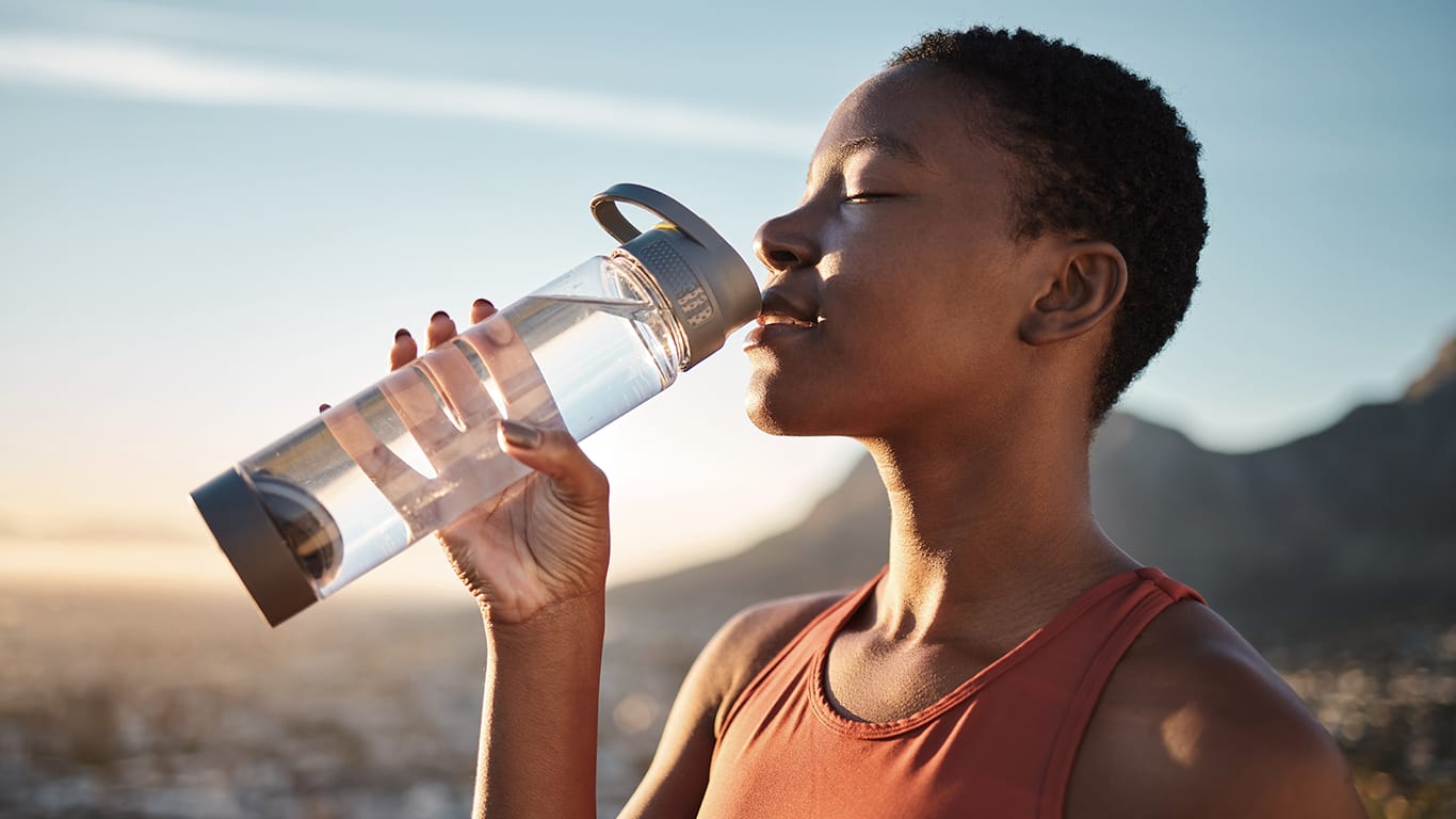 Woman runner drinking water for body detox during an outdoor workout.