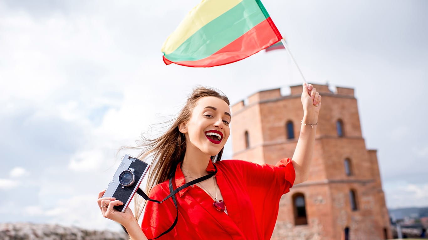 Portrait of a young female tourist with lithuanian flag in front of the famous old tower in Vilnius. Woman having great vacations in Lithuania.
