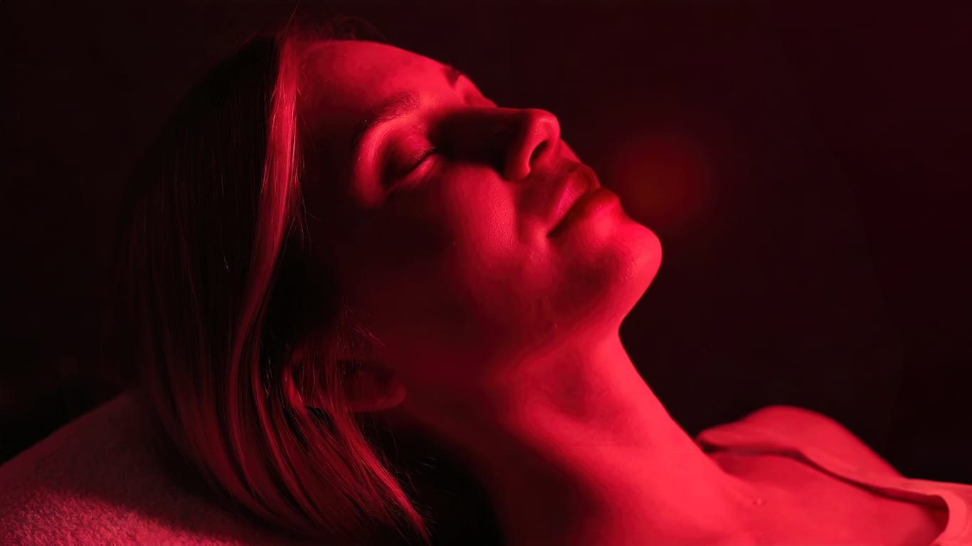 A woman reclines, enjoying red light therapy for wellness or cosmetic treatment. Female appears tranquil under the therapeutic glow, likely seeking rejuvenation or healing..