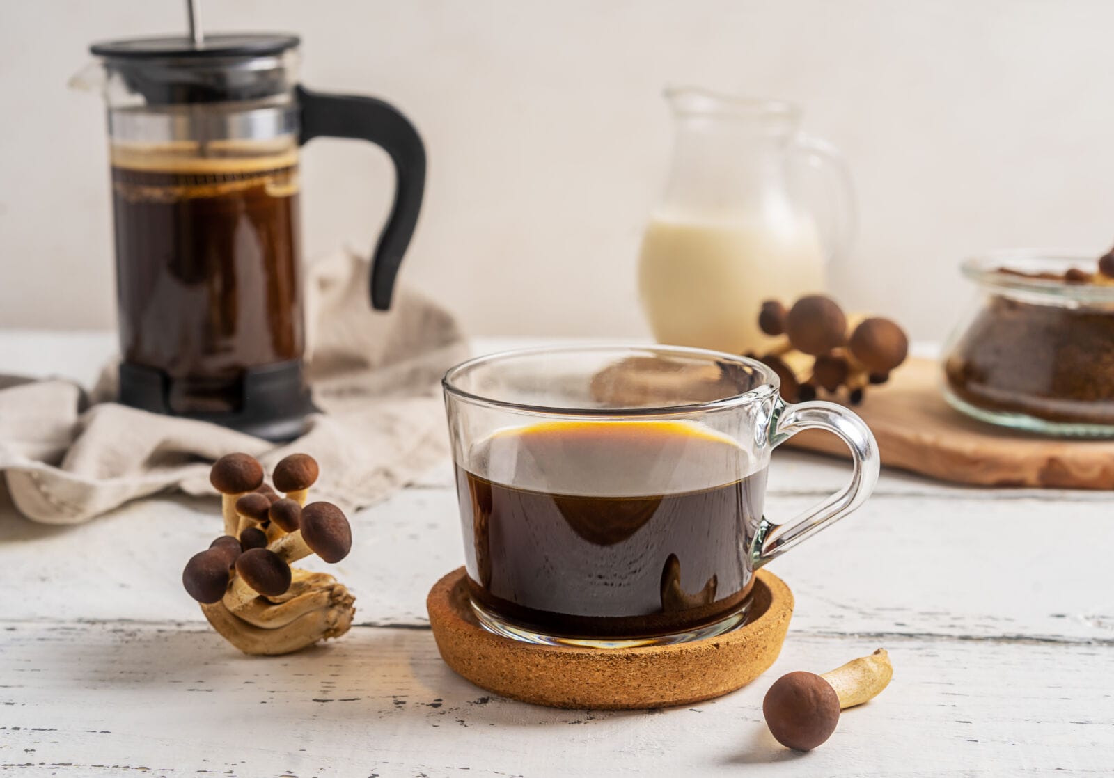 Healthy trendy coffee with mushrooms in cup, coffee pot with milk jar and mix of coffee and dried mushrooms on white wooden background.