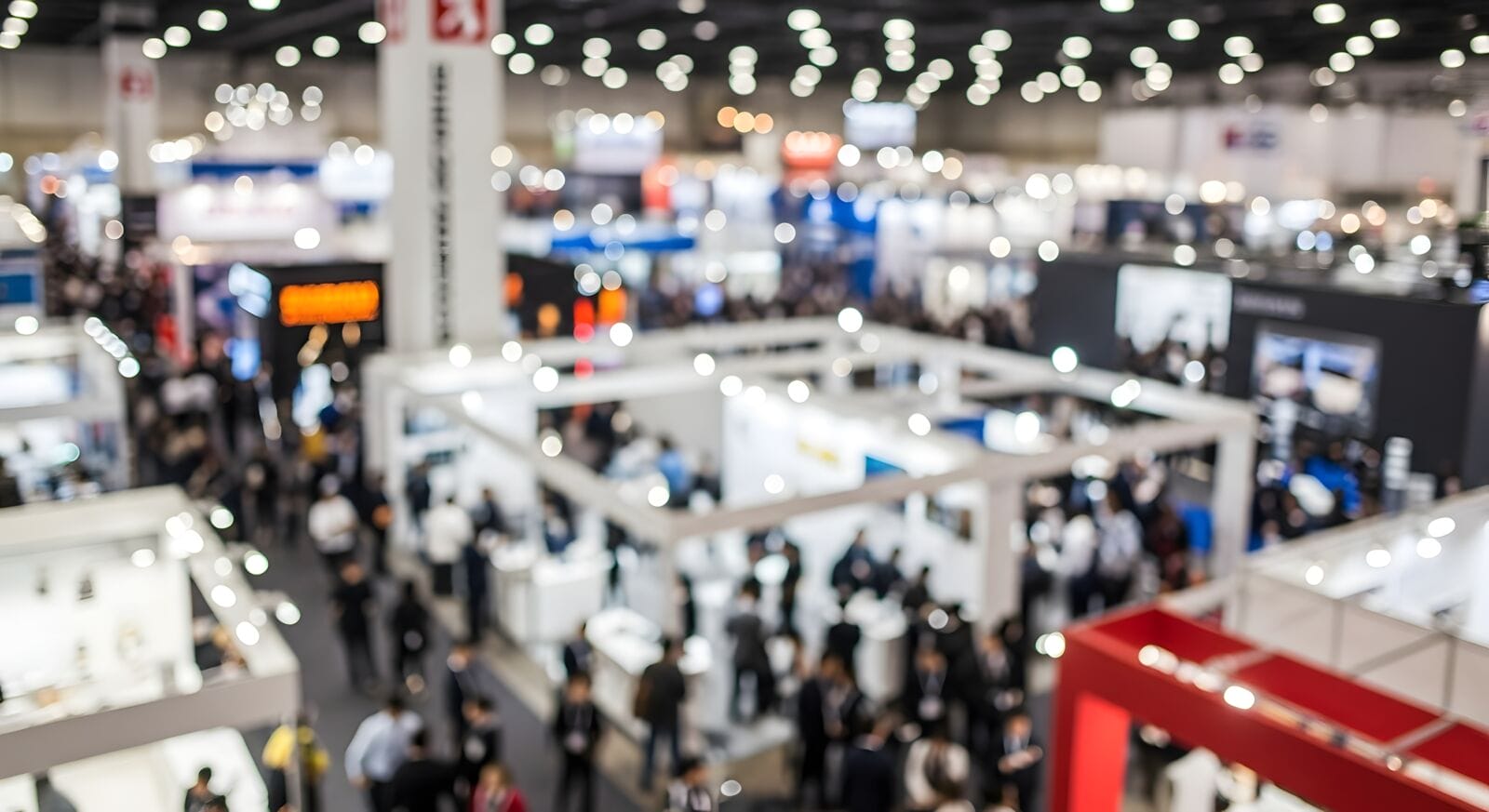 High angle shot of large convention center floor filled with display stands and attendees at busy commercial industry event.