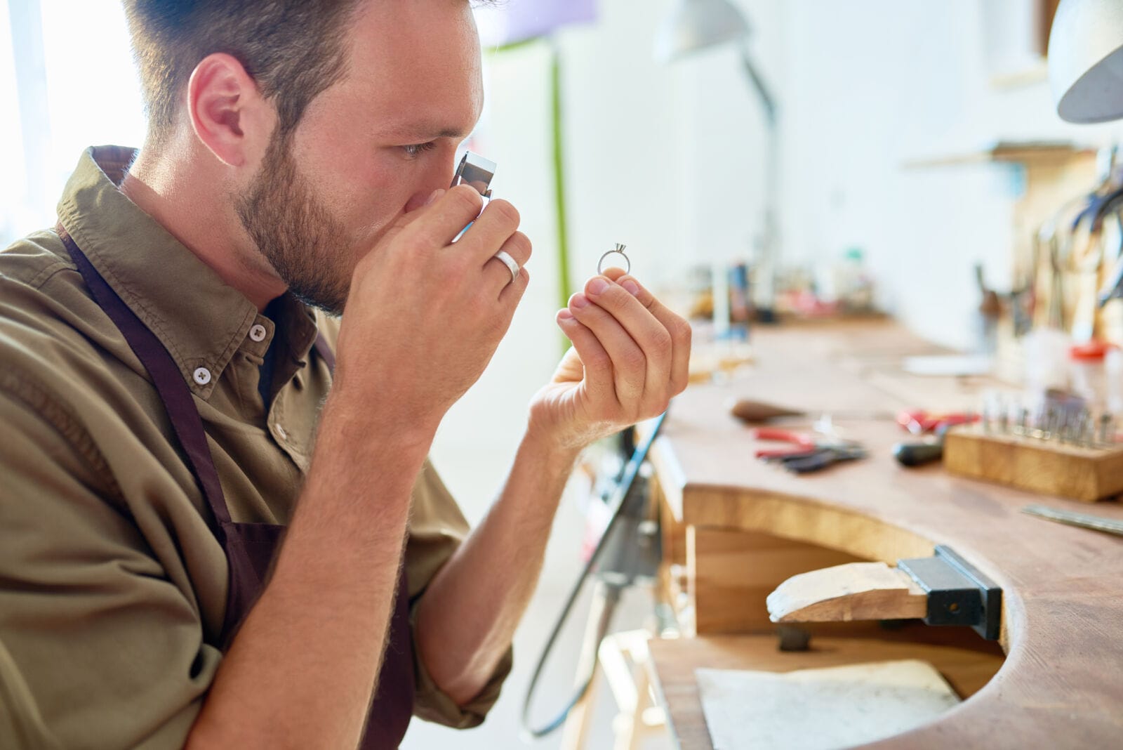 Side view portrait of jeweler inspecting ring through magnifying glass in workshop.